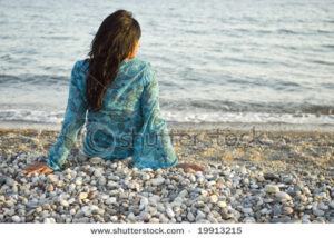 stock-photo-a-rear-view-of-a-beautiful-indian-girl-sitting-alone-on-a-beach-and-looking-out-to-sea-19913215