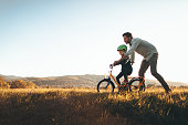 Photo of a young boy and his father on a bicycle lane, learning to ride a bike.